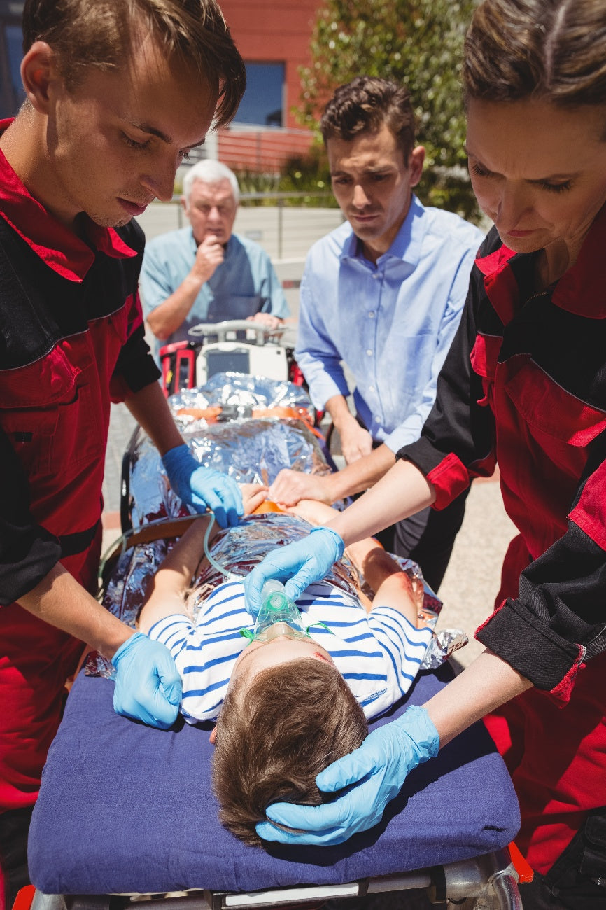Paramedics stabilizing a pediatric patient on a stretcher with an oxygen mask