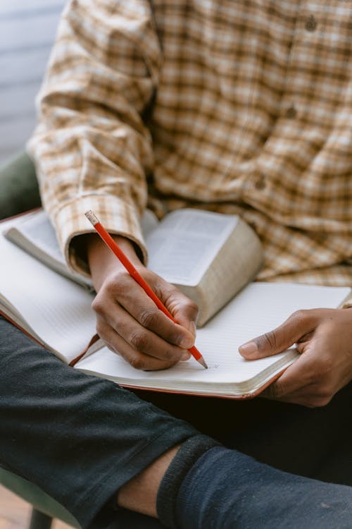 Person in plaid shirt writing notes in a notebook during NREMT test prep