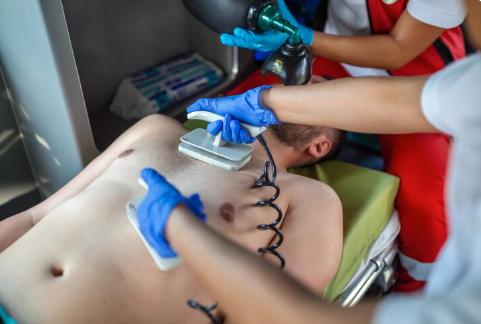 EMS paramedics providing assisted ventilation to a patient using a noninvasive mask near an ambulance