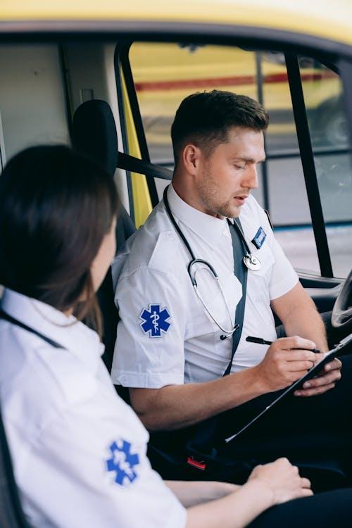 Paramedics inside an ambulance, one recording patient information on a clipboard during emergency care