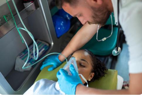 An EMT providing ventilations to a patient with a bag-valve mask (BVM) while a paramedic monitors vitals inside an ambulance