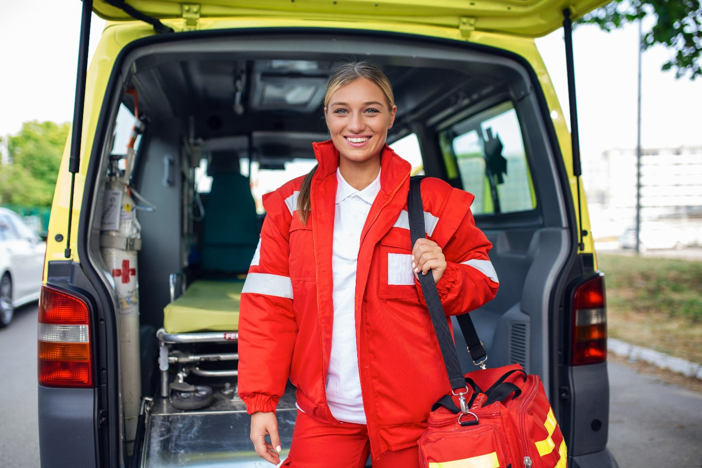 Smiling EMT standing at the back of an ambulance holding a trauma bag