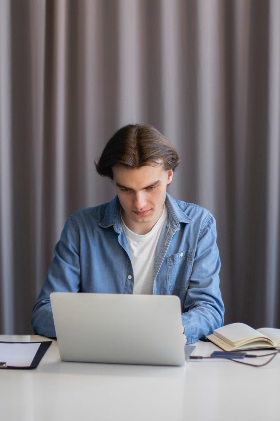 A man studying at home using a laptop and notes to prepare for the NREMT exam