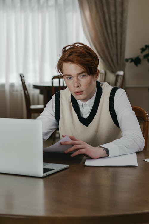 A man using a laptop with papers on the table, preparing for the NREMT exam