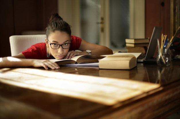  A tired young female student preparing for NREMT exam prep at home with books and notes.