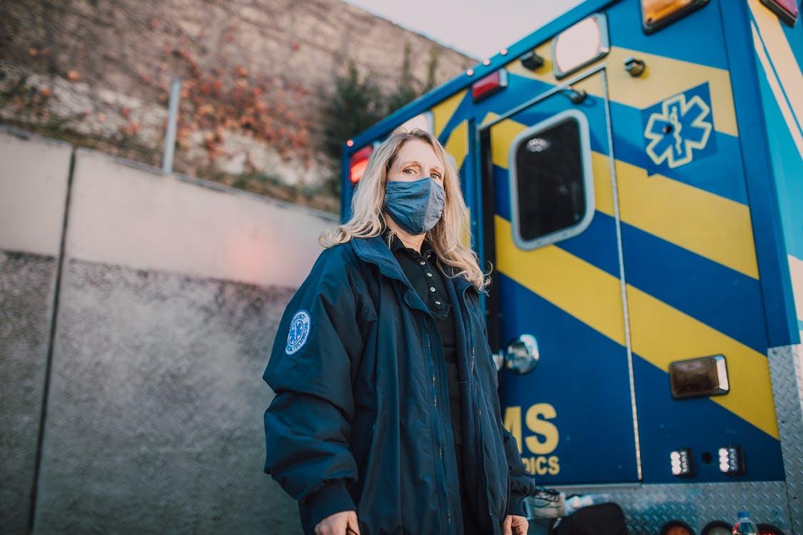 A female EMT wearing a mask standing behind an ambulance.
