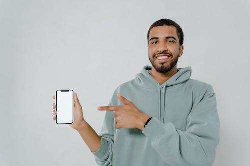 Man in a gray hoodie holding a smartphone, using an NREMT app for NREMT exam preparation