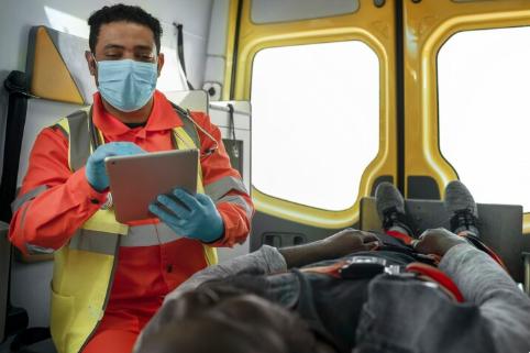 Paramedic using a tablet beside a patient in the back of an ambulance