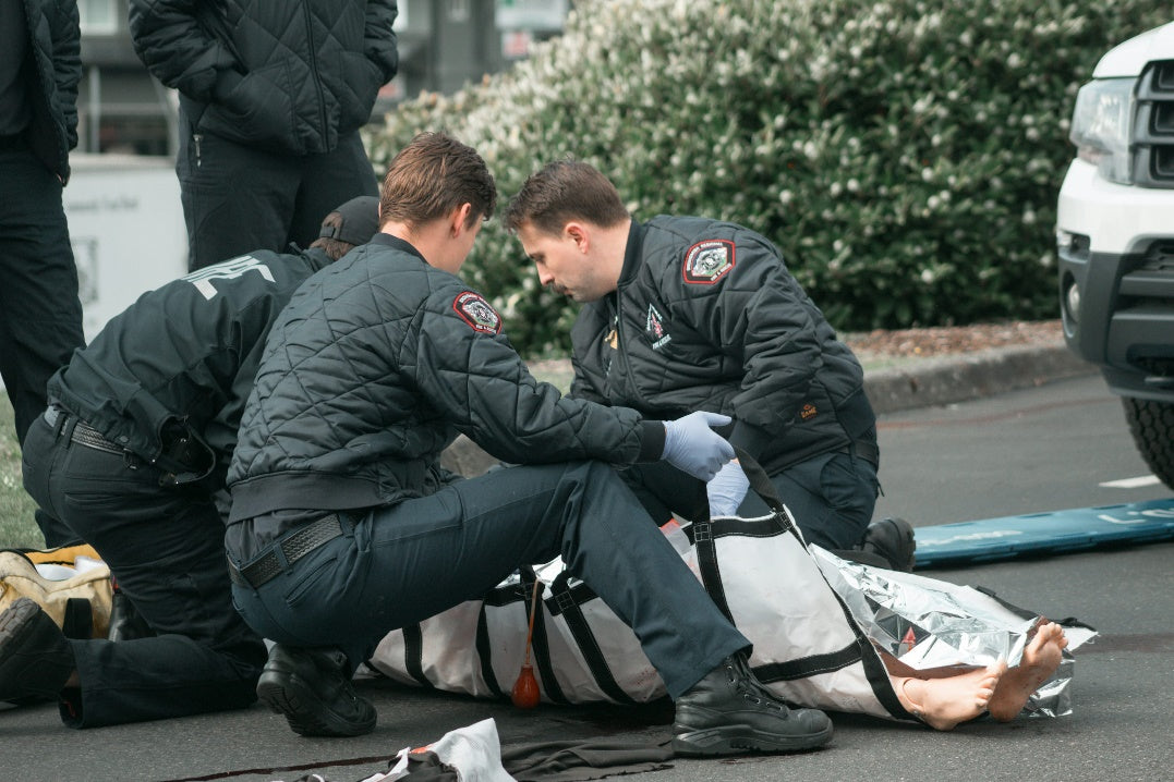 Two paramedics in uniform sitting on the ground during an EMS training break