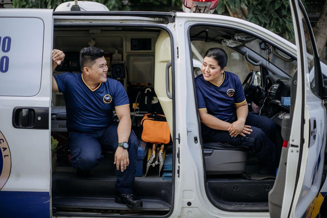 Two paramedics, a man and a woman, sitting inside an ambulance preparing for an emergency call