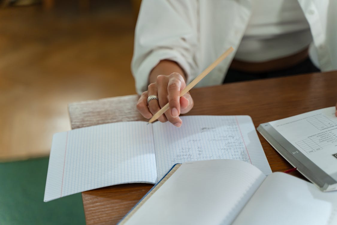 Person sitting at a wooden table holding a pencil