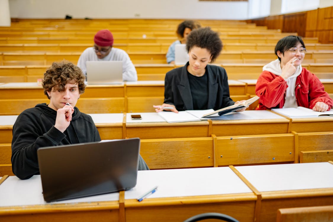 A group of students in a lecture hall, working on laptops and taking notes during a class session.