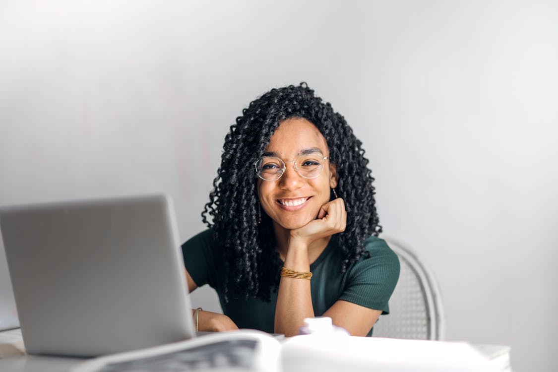 A woman sitting at a table with a laptop, smiling while studying for the NREMT exam.