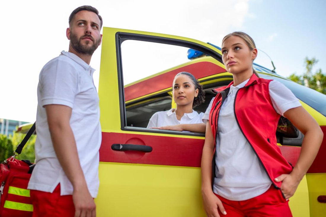 Three paramedics standing in front of an ambulance, one carrying a medical trauma bag, discussing patient care