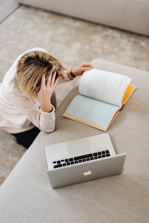A woman reading a book with an open laptop on the table, preparing for the NREMT exam.
